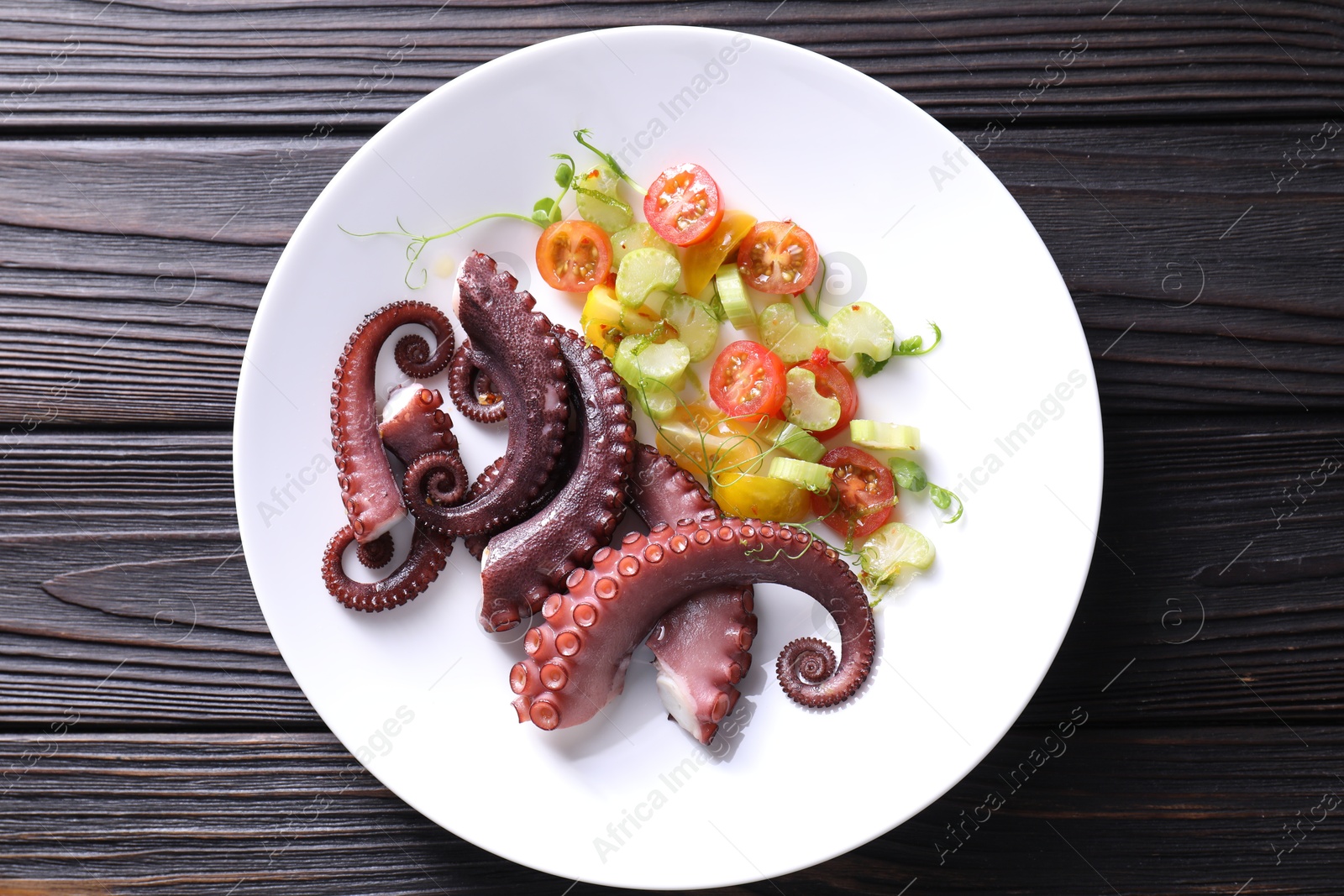 Photo of Plate with tasty boiled octopus tentacles and salad on wooden table, top view