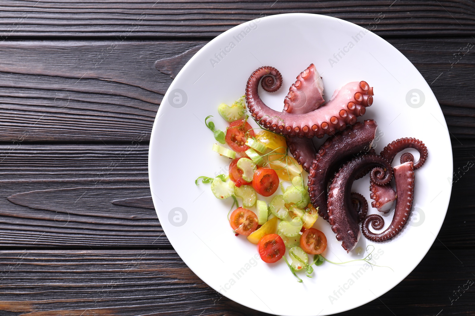 Photo of Plate with tasty boiled octopus tentacles and salad on wooden table, top view. Space for text