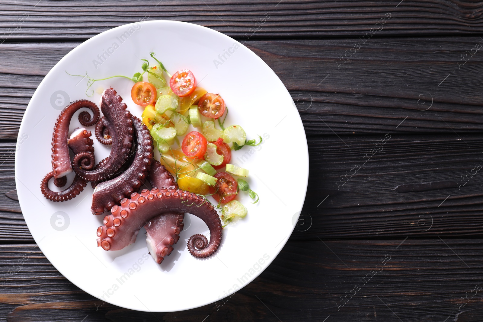 Photo of Plate with tasty boiled octopus tentacles and salad on wooden table, top view. Space for text