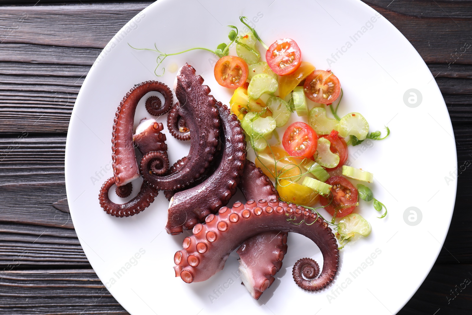 Photo of Plate with tasty boiled octopus tentacles and salad on wooden table, top view