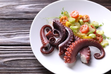 Photo of Plate with tasty boiled octopus tentacles and salad on wooden table, closeup