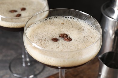 Glasses of delicious espresso martini and coffee beans on table, closeup