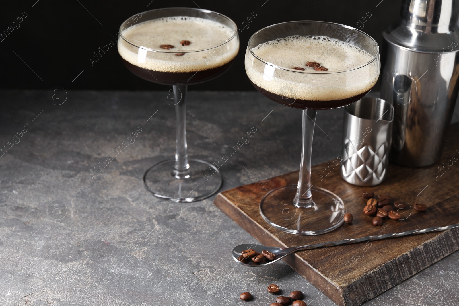 Photo of Glasses of delicious espresso martini and coffee beans on dark textured table, closeup. Space for text