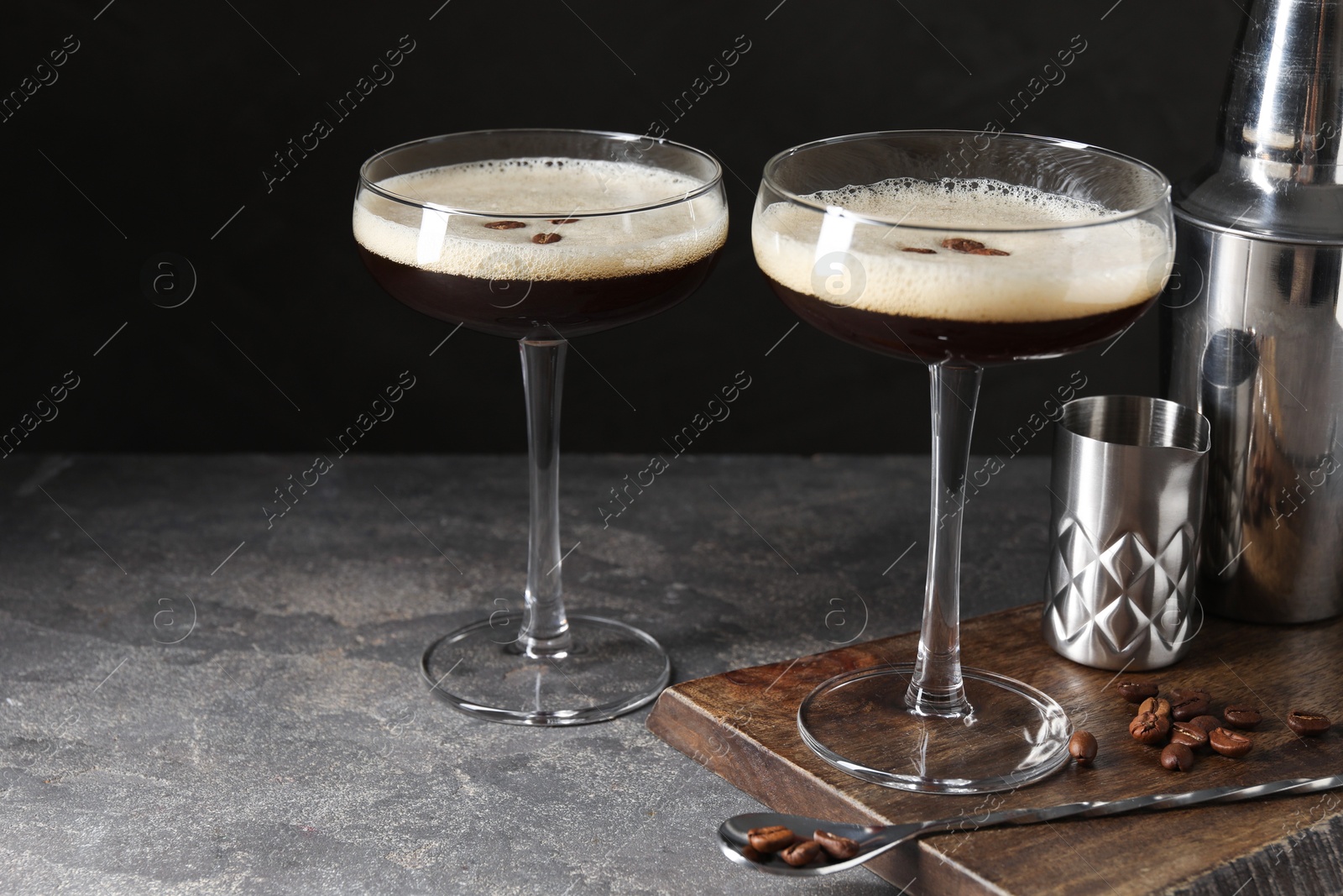 Photo of Glasses of delicious espresso martini and coffee beans on dark textured table, closeup. Space for text