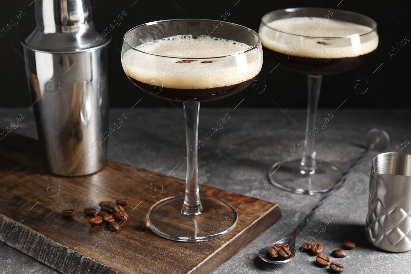 Photo of Glasses of delicious espresso martini, shaker and coffee beans on dark textured table, closeup