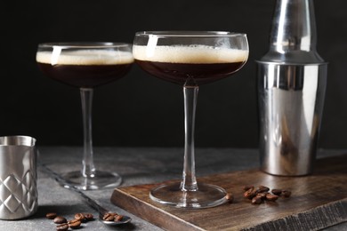 Photo of Glasses of delicious espresso martini, shaker and coffee beans on dark textured table, closeup