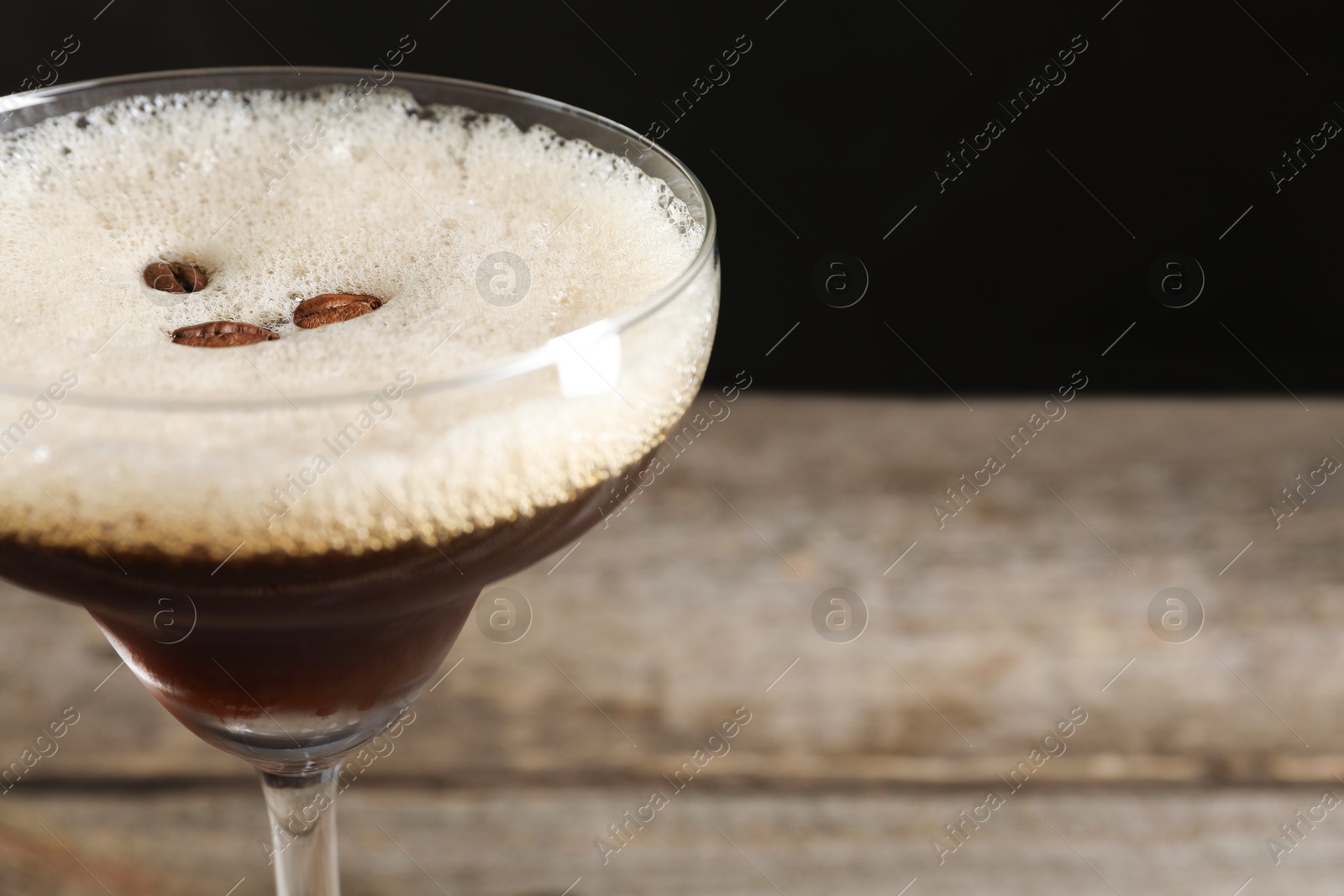 Photo of Delicious espresso martini with coffee beans in glass on blurred background, closeup. Space for text