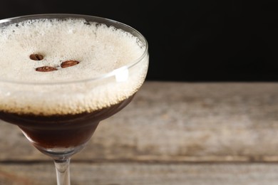 Photo of Delicious espresso martini with coffee beans in glass on blurred background, closeup. Space for text