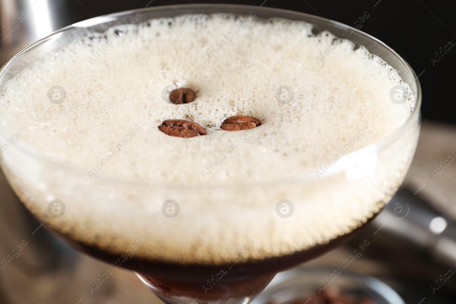 Photo of Delicious espresso martini with coffee beans in glass on blurred background, closeup