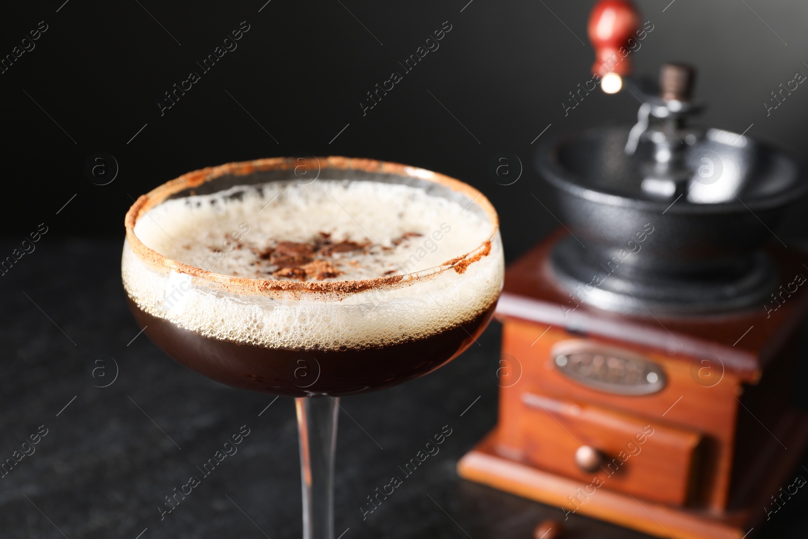 Photo of Glass of delicious espresso martini and manual grinder on blurred background, closeup