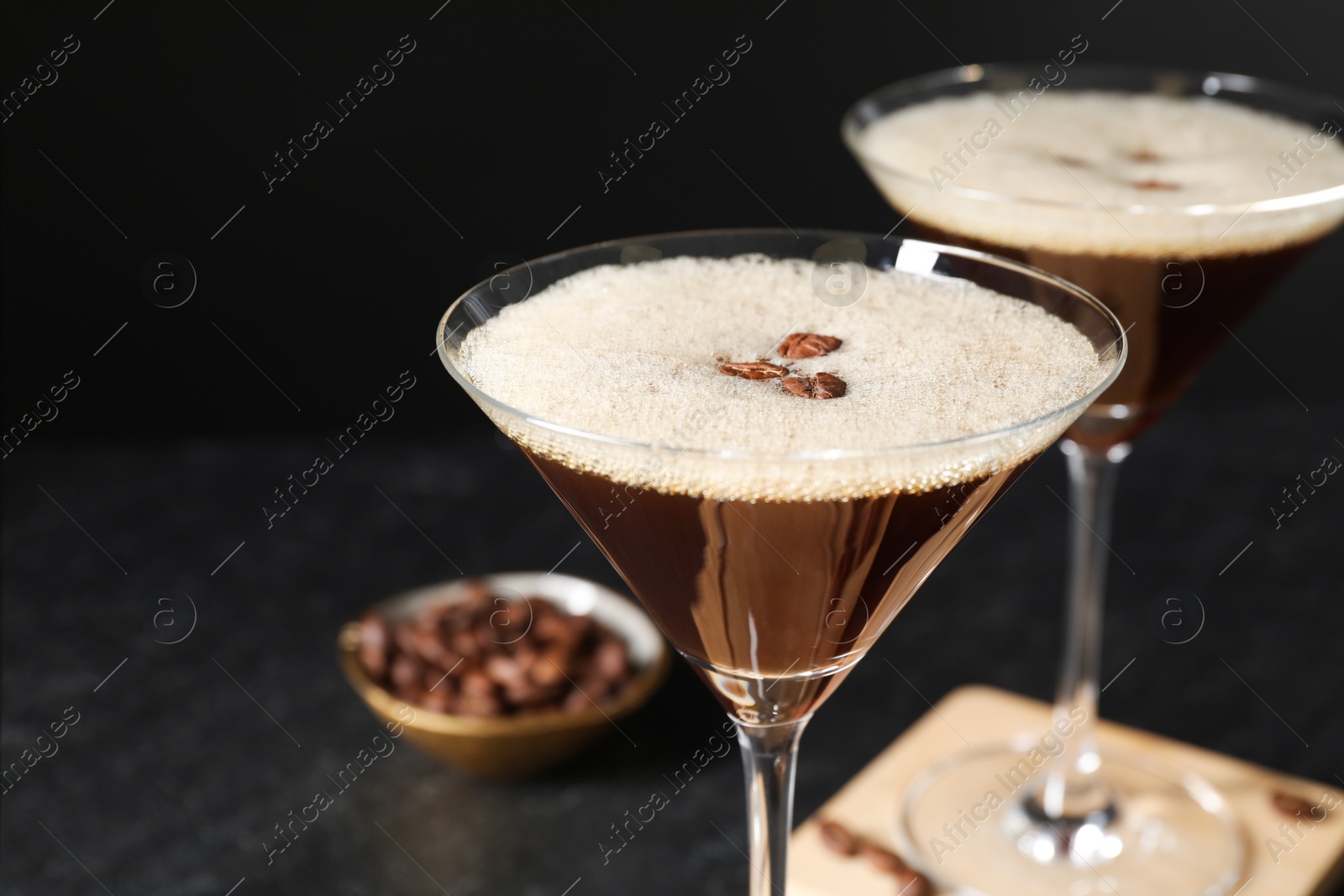 Photo of Delicious espresso martini with coffee beans in glasses on blurred black background, closeup