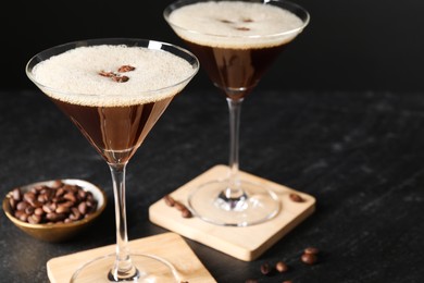 Photo of Glasses of delicious espresso martini and coffee beans on dark textured table, closeup