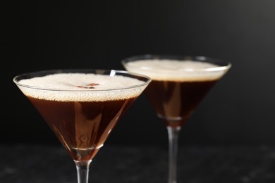 Photo of Delicious espresso martini in glasses on blurred black background, closeup