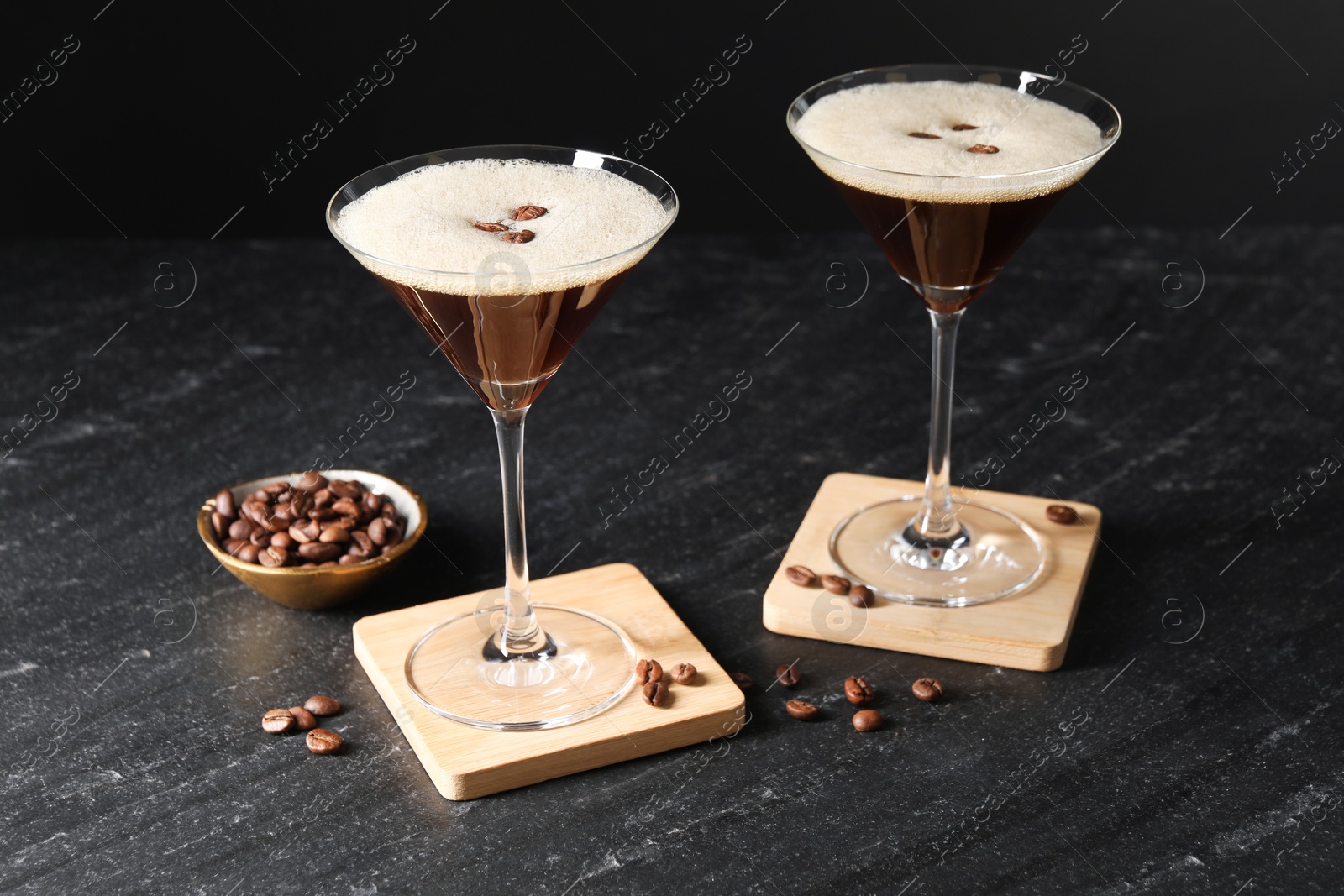 Photo of Glasses of delicious espresso martini and coffee beans on dark textured table