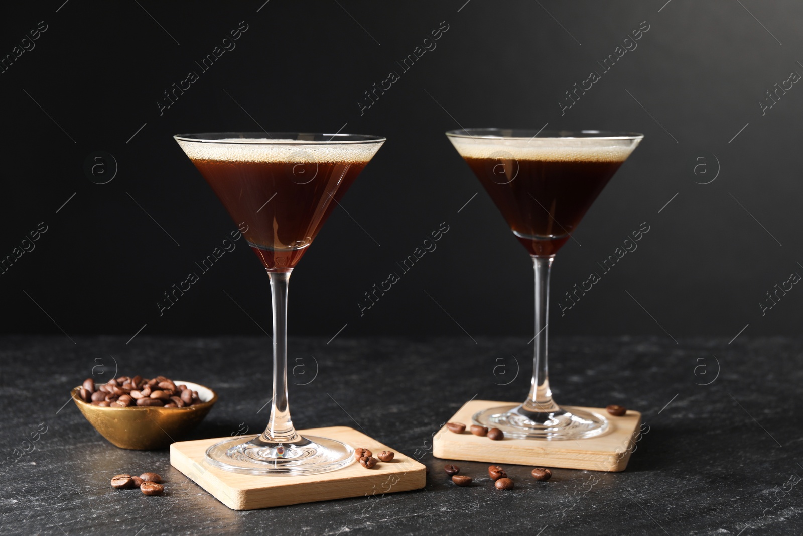 Photo of Glasses of delicious espresso martini and coffee beans on dark textured table