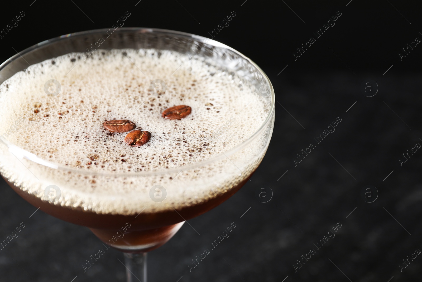 Photo of Delicious espresso martini with coffee beans in glass on blurred black background, closeup