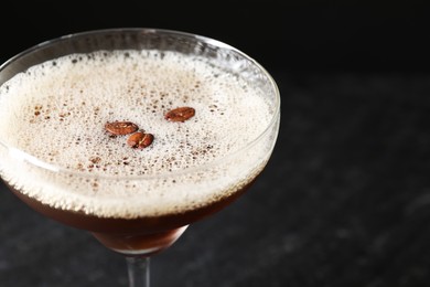 Photo of Delicious espresso martini with coffee beans in glass on blurred black background, closeup