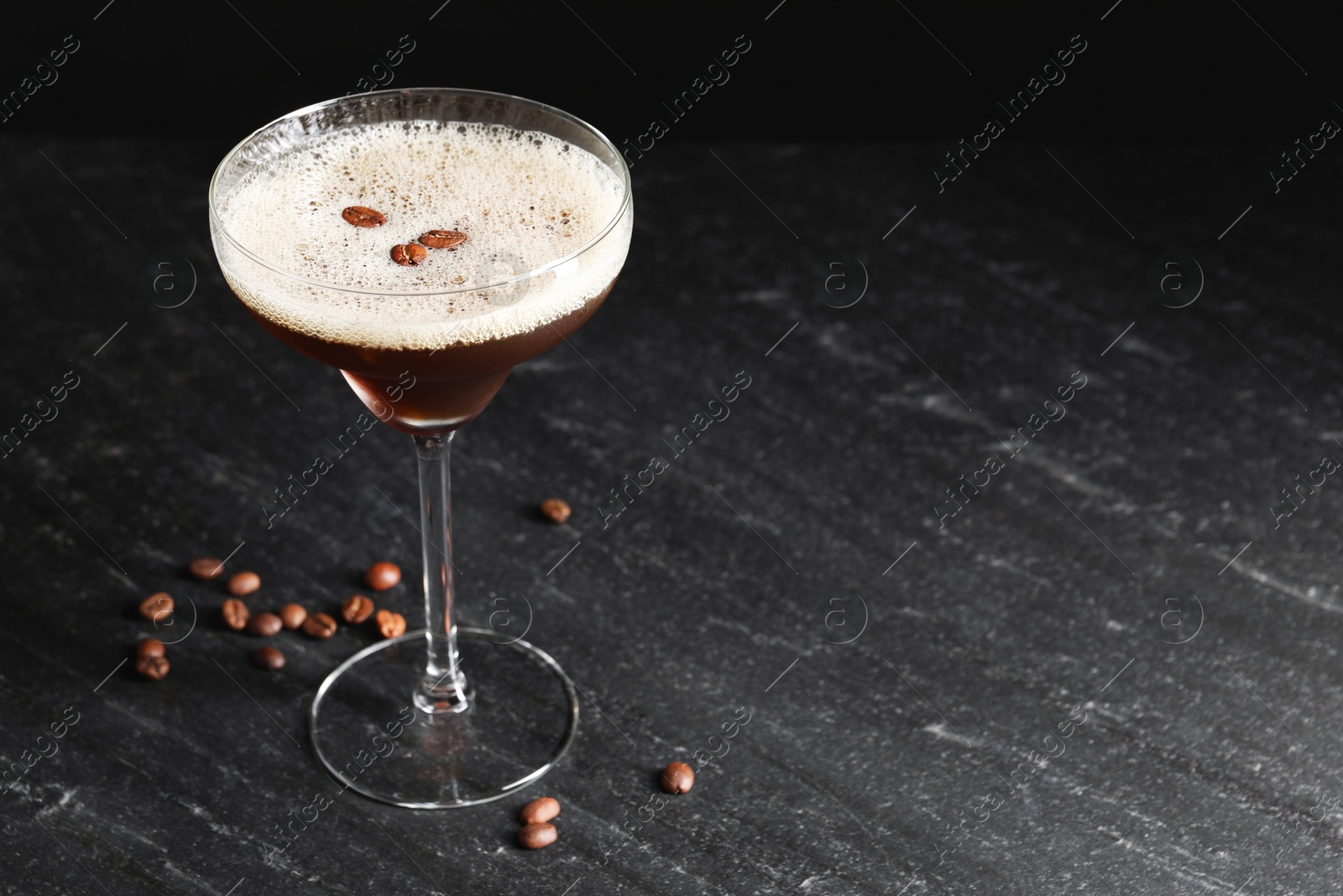 Photo of Glass of delicious espresso martini and coffee beans on dark textured table, closeup. Space for text