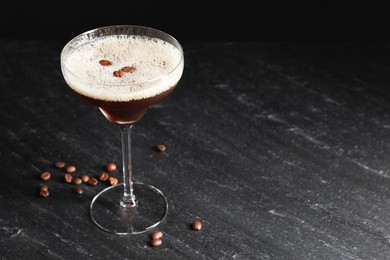 Photo of Glass of delicious espresso martini and coffee beans on dark textured table, closeup. Space for text