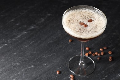 Photo of Glass of delicious espresso martini and coffee beans on dark textured table, closeup. Space for text