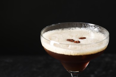 Photo of Delicious espresso martini with coffee beans in glass on black background, closeup