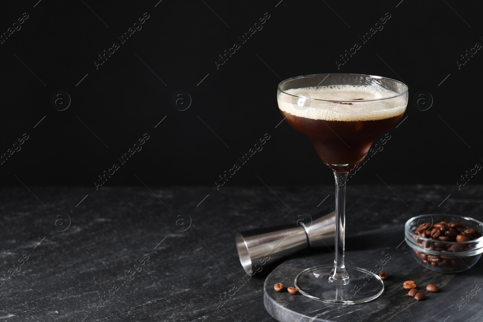 Photo of Glasses of delicious espresso martini, jigger and coffee beans on dark textured table, closeup. Space for text