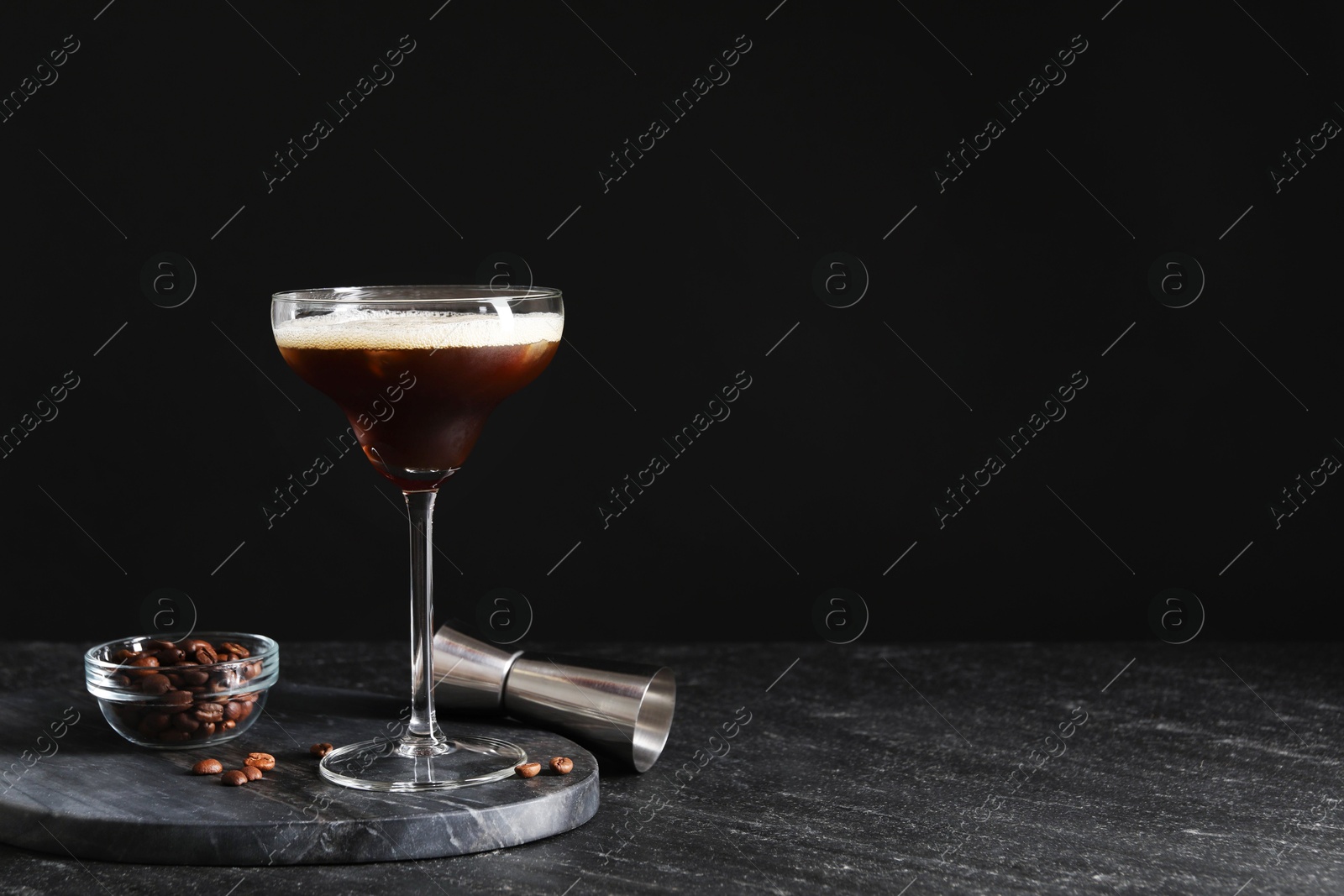 Photo of Glasses of delicious espresso martini, jigger and coffee beans on dark textured table, closeup. Space for text