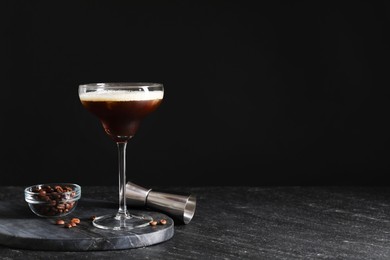 Photo of Glasses of delicious espresso martini, jigger and coffee beans on dark textured table, closeup. Space for text