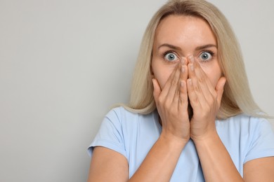 Portrait of scared woman on gray background, space for text