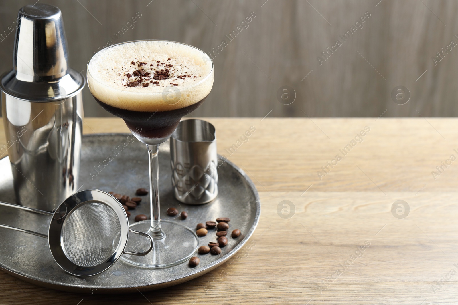 Photo of Tray with delicious espresso martini in glass, sieve, shaker and coffee beans on wooden table. Space for text