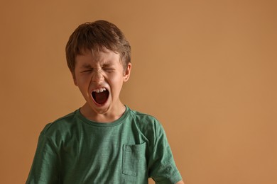 Photo of Scared little boy screaming on beige background. Space for text