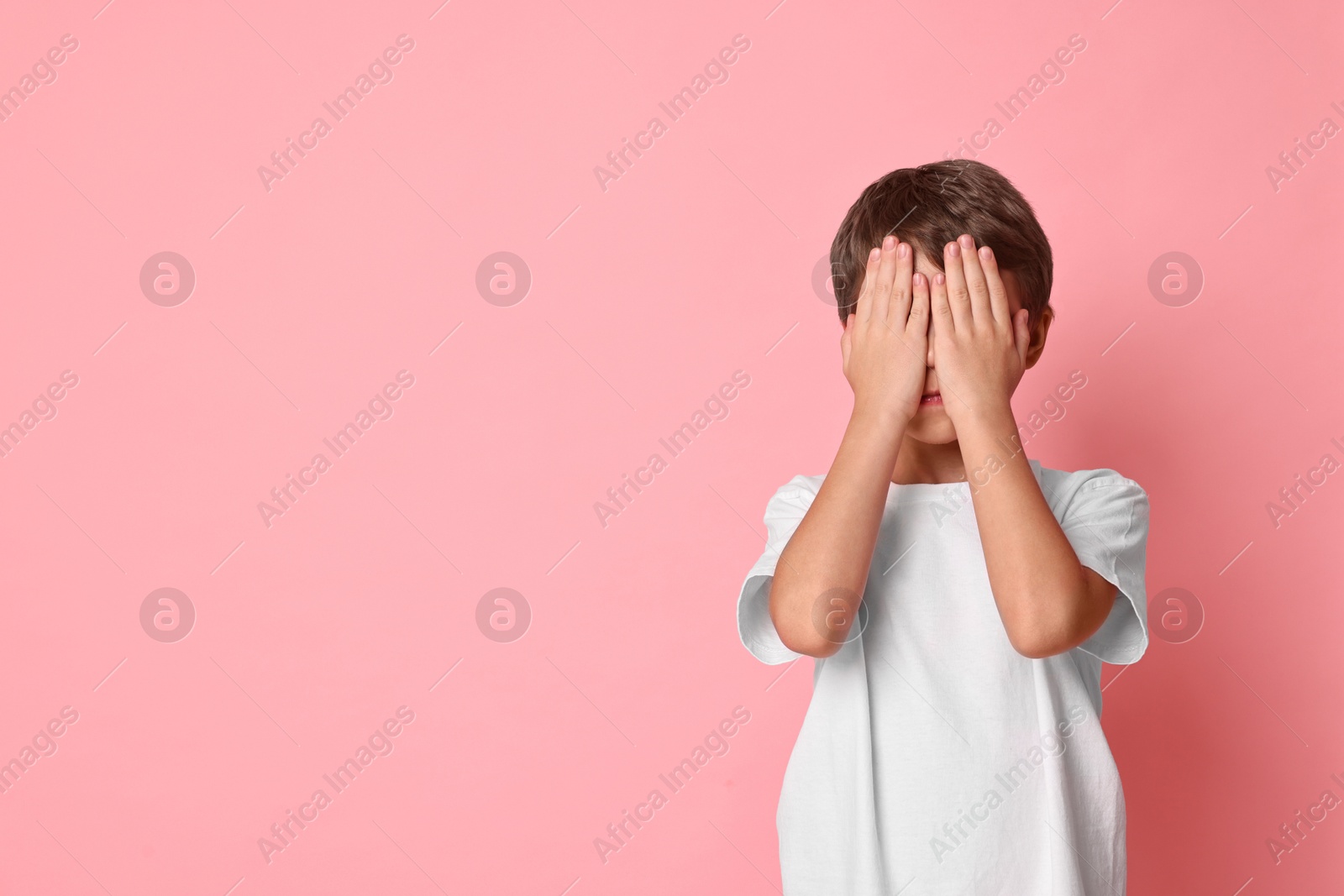 Photo of Scared little boy covering face on pink background. Space for text