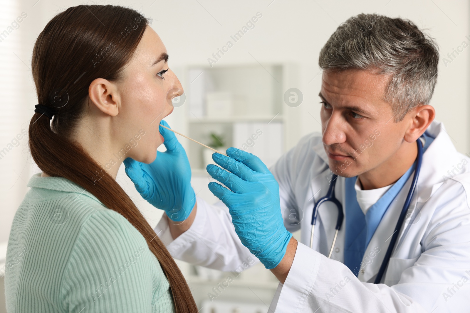 Photo of Doctor examining woman's throat with tongue depressor in clinic