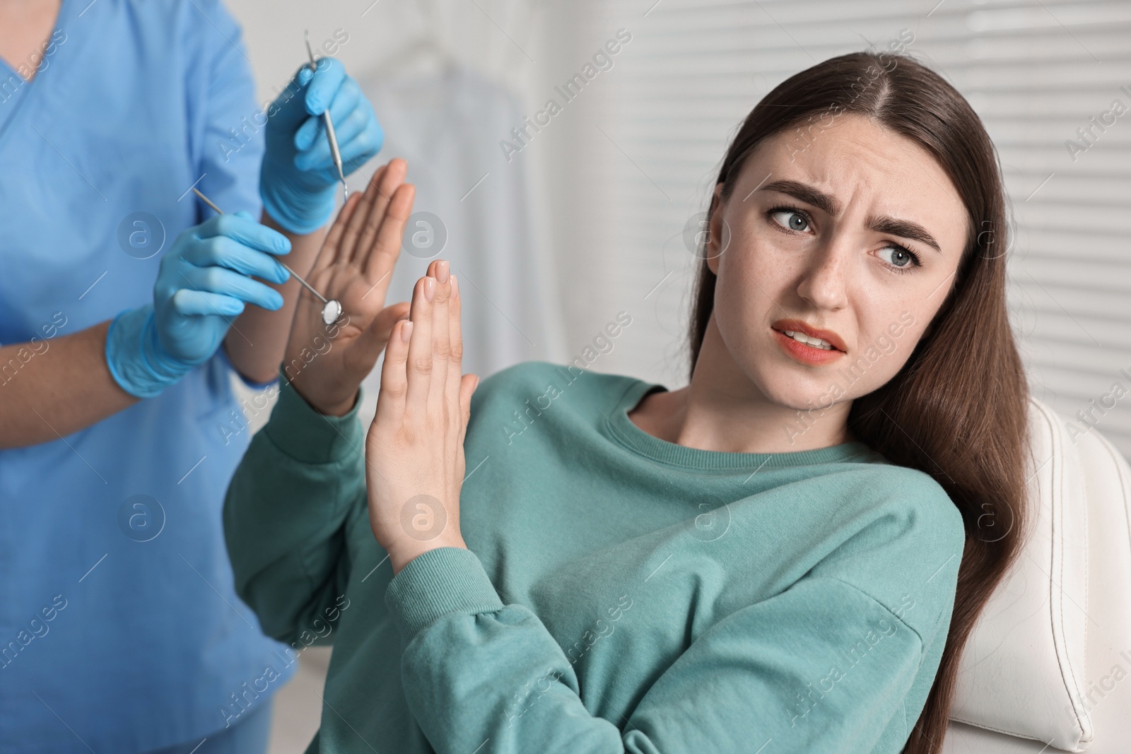 Photo of Dental phobia. Dentist working with scared woman in clinic, closeup