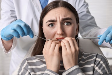 Photo of Dental phobia. Dentist working with scared woman in clinic, closeup