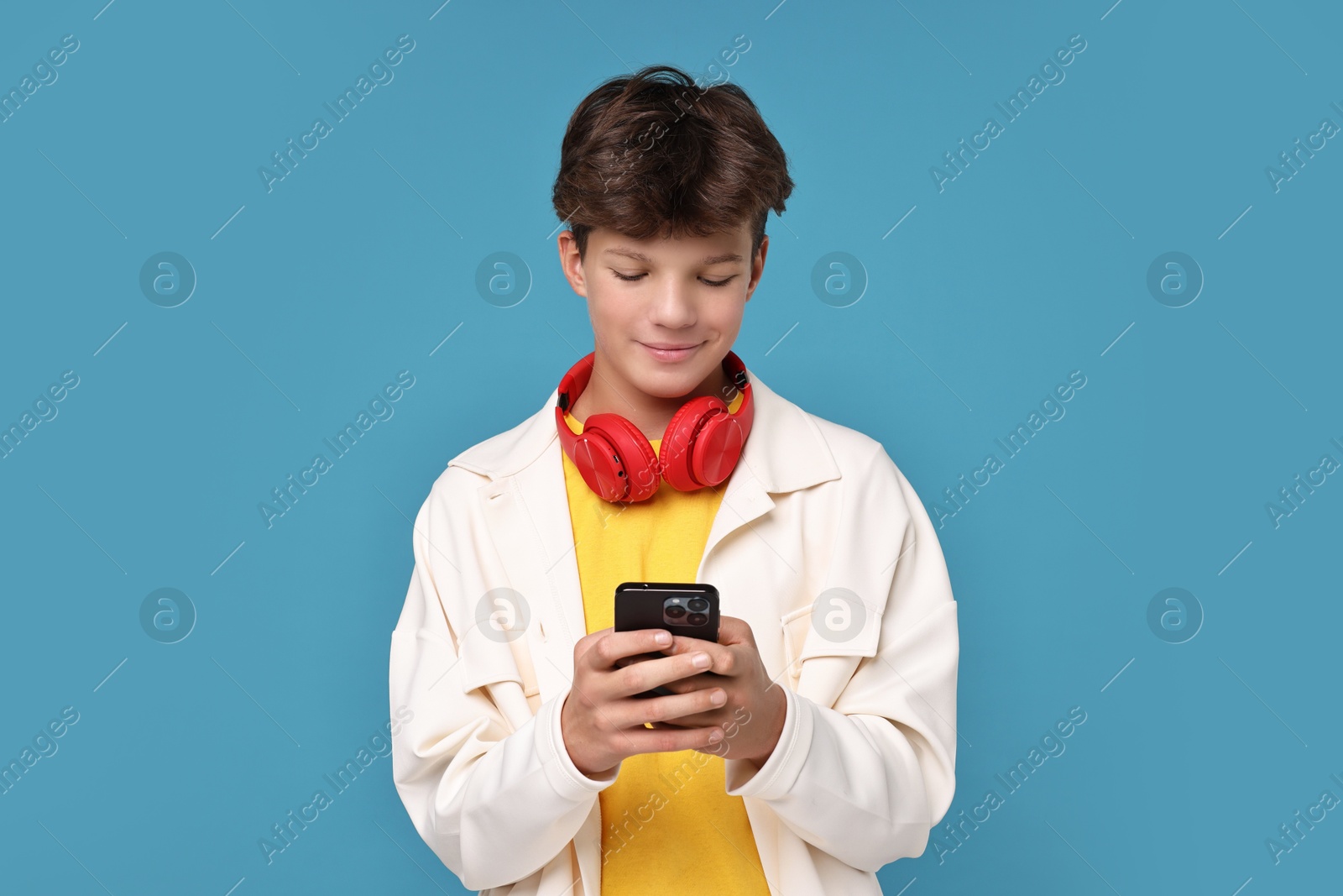 Photo of Teenage boy with headphones and smartphone on light blue background