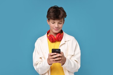 Photo of Teenage boy with headphones and smartphone on light blue background