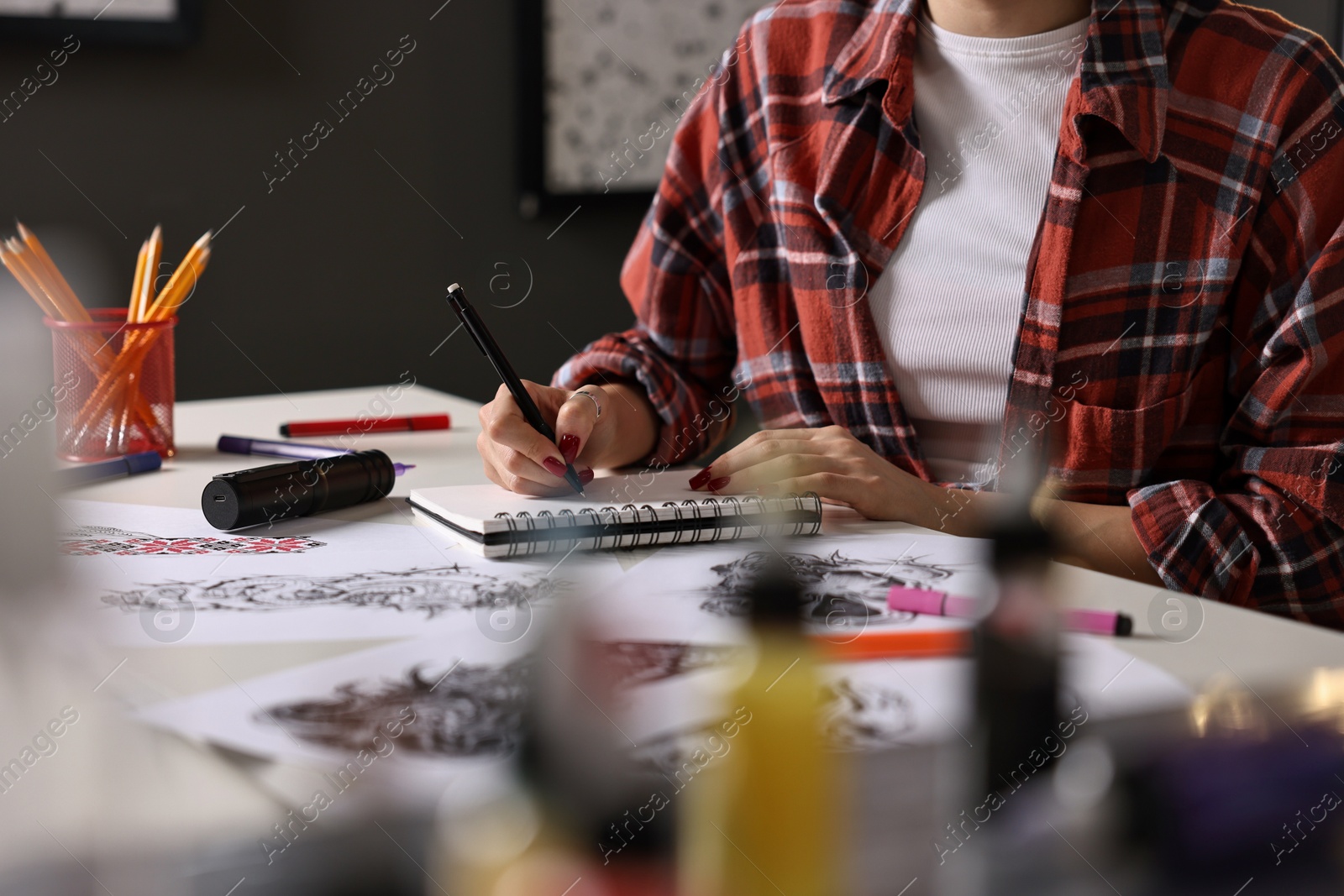 Photo of Tattoo artist drawing sketch with pen at white table, closeup