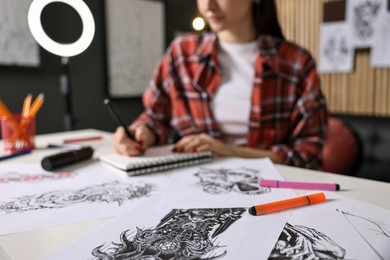 Photo of Tattoo artist drawing sketch with pen at white table in salon, selective focus