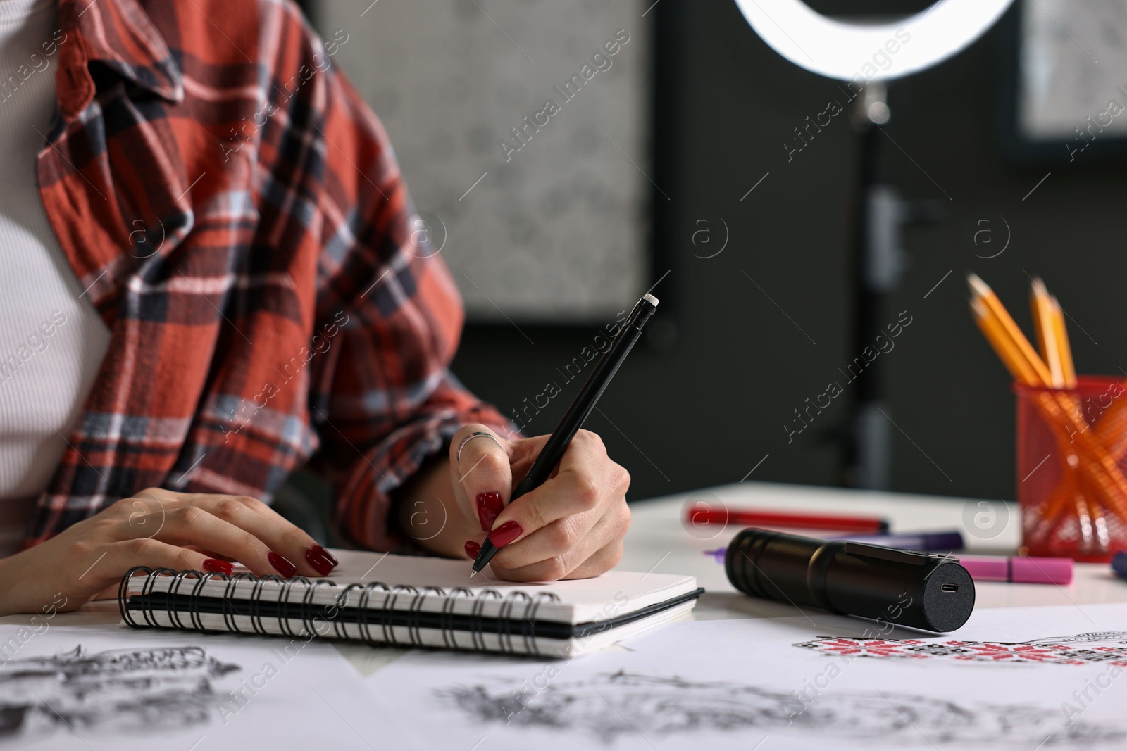 Photo of Tattoo artist drawing sketch with pen at table in salon, closeup