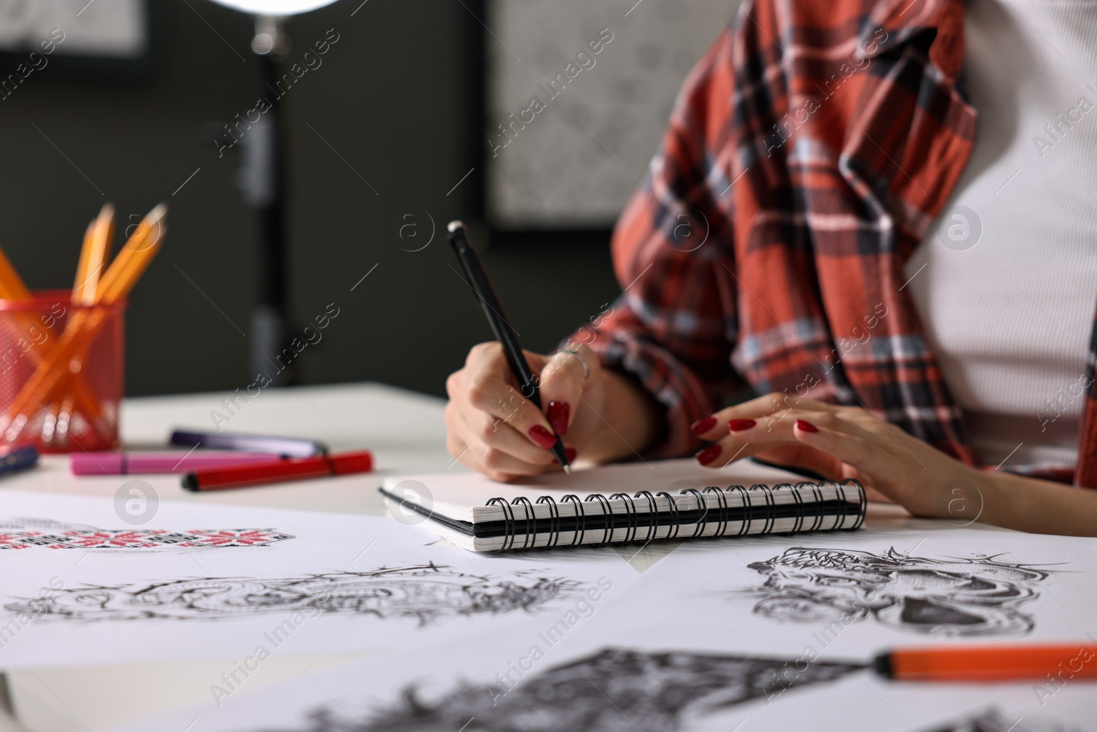 Photo of Tattoo artist drawing sketch with pen at table in salon, closeup