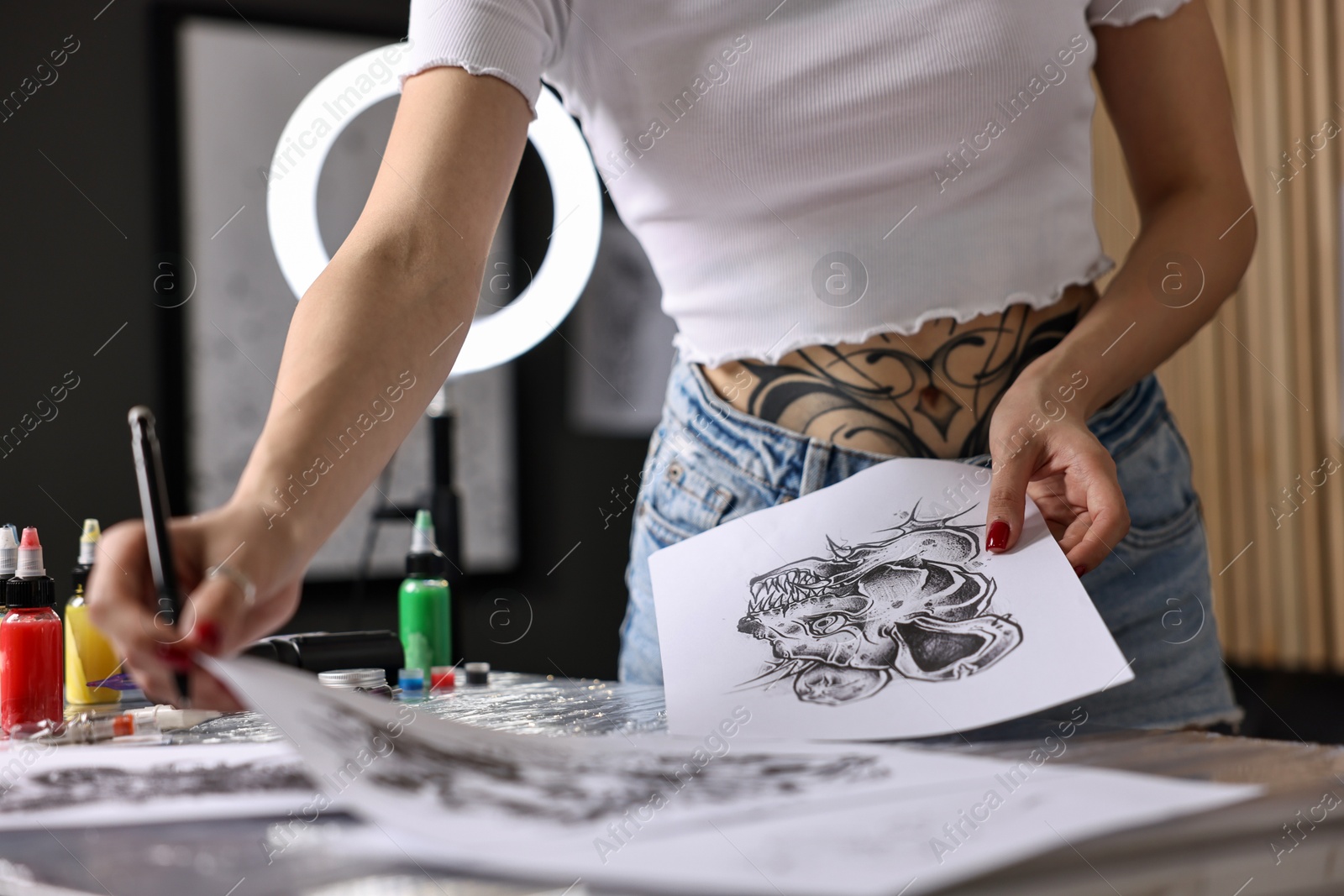 Photo of Tattoo artist working with sketches at table in salon, closeup