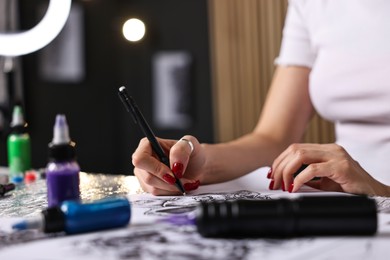 Photo of Tattoo artist drawing sketch at table with supplies in salon, closeup