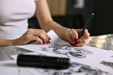 Photo of Tattoo artist drawing sketch at table with supplies in salon, closeup