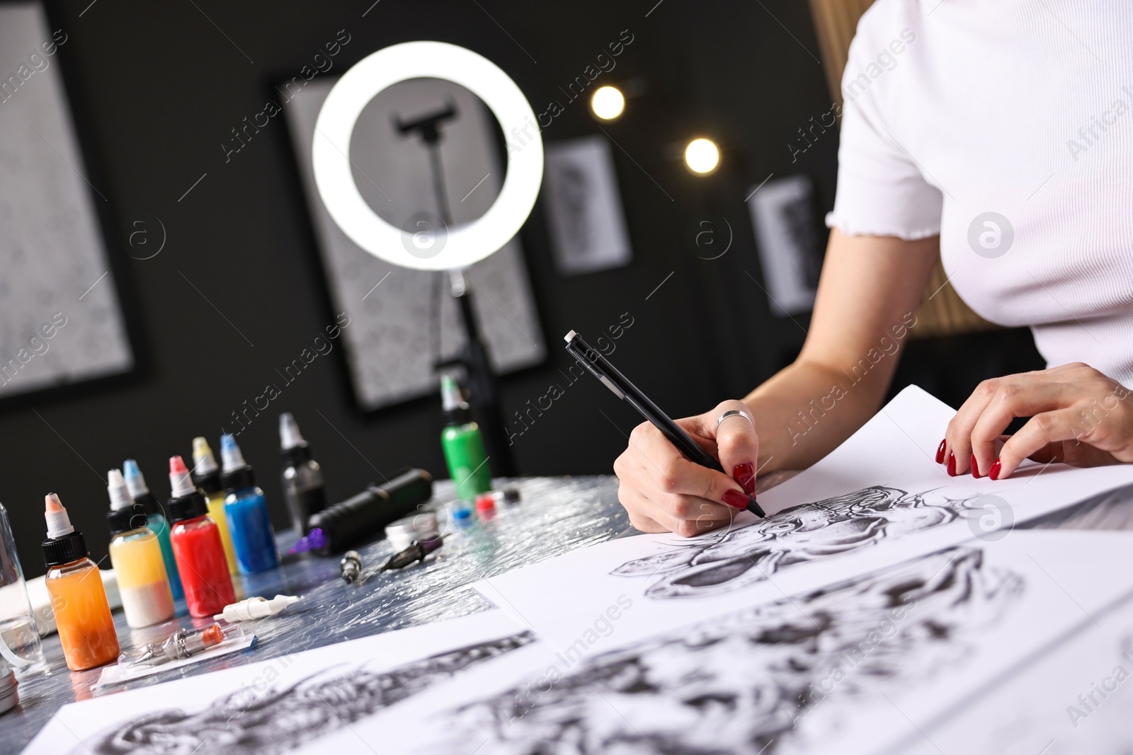 Photo of Tattoo artist drawing sketch at table with supplies in salon, closeup