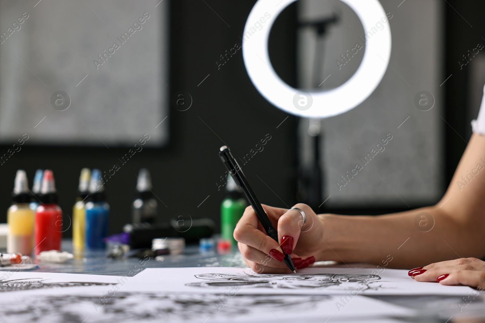 Photo of Tattoo artist drawing sketch at table with supplies in salon, closeup