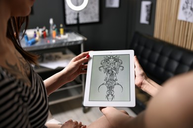 Photo of Tattoo artist showing tablet with sketch to client in salon, closeup