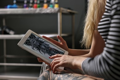 Tattoo artist showing tablet with sketch to client in salon, closeup