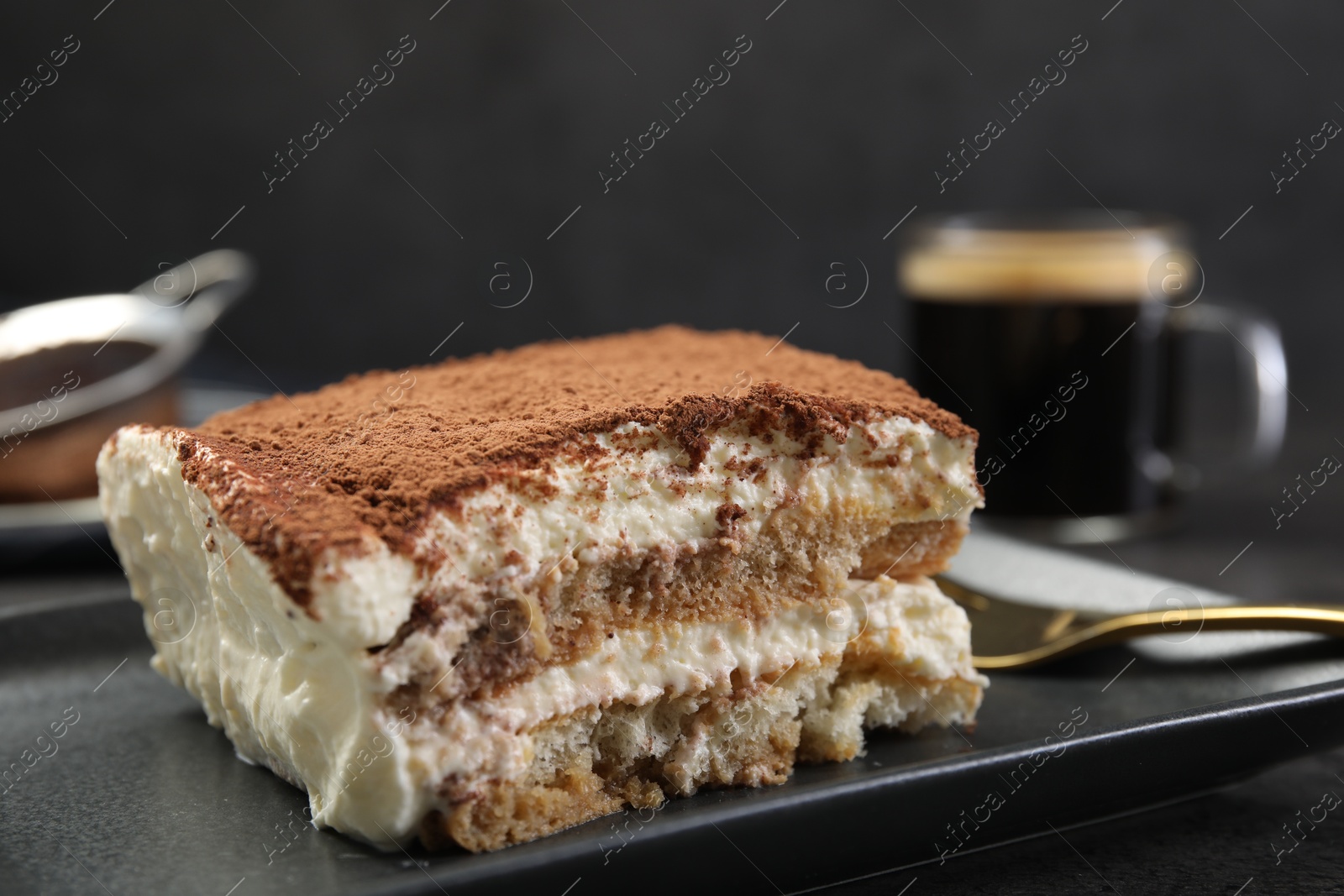 Photo of Piece of tasty tiramisu on black table, closeup