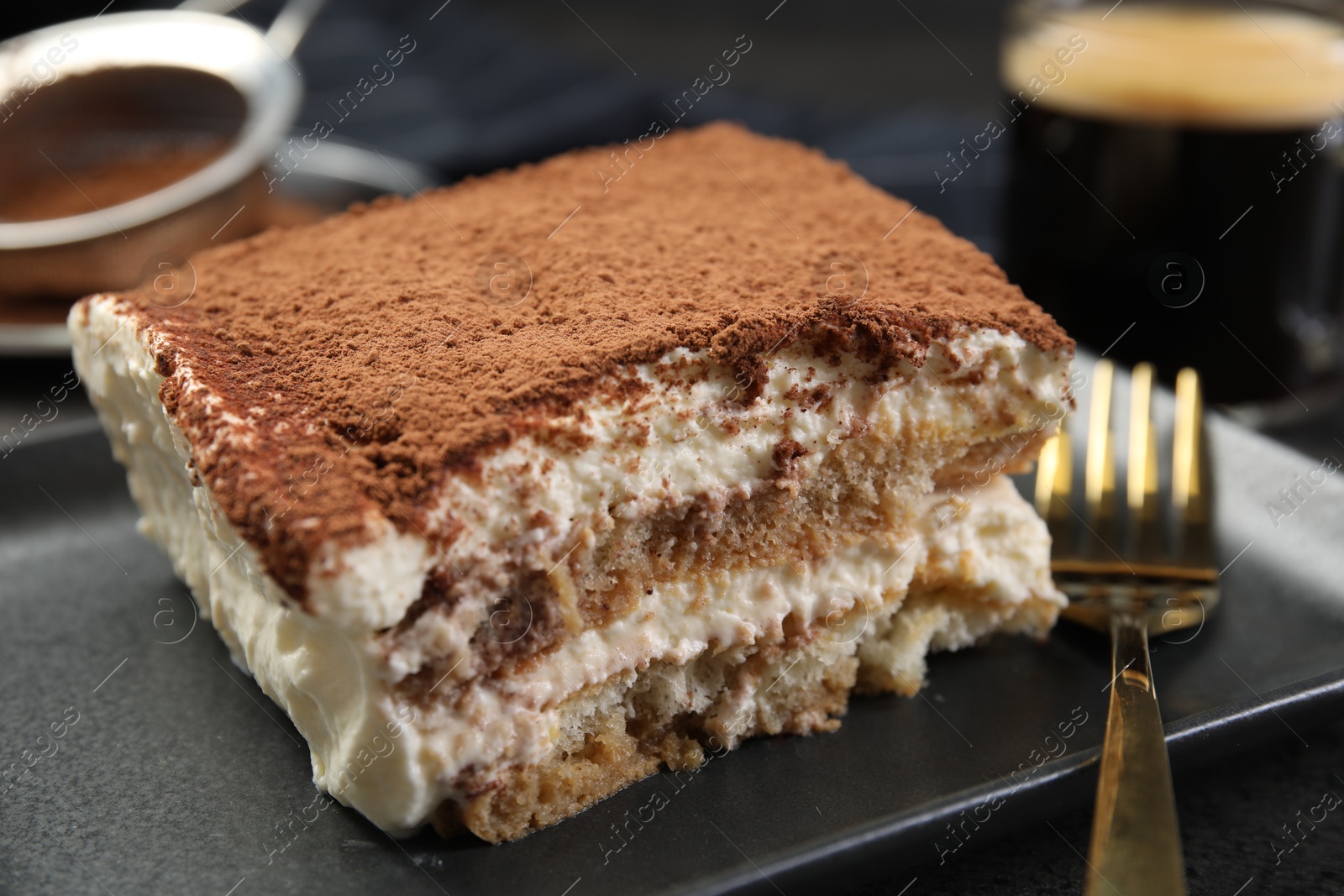 Photo of Piece of tasty tiramisu and fork on black table, closeup